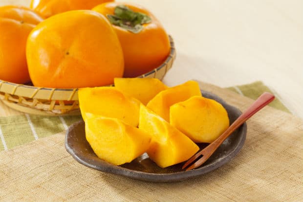 кусочки хурмы на тарелке и целые фрукты