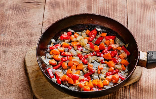обжаренные кусочки лука, перца и моркови на сковороде на разделочной доске на столе