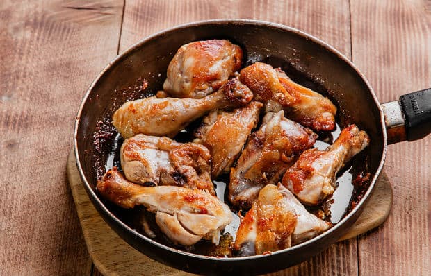 жареные кусочки курицы в сковороде на разделочной доске на столе