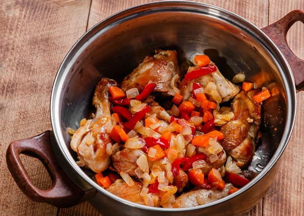 кусочки жареной курицы с морковкой, перцем и луком в кастрюле на столе