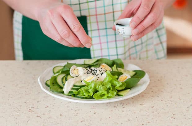 вареные перепелиные яйца с кусочками зелени и огурцов со сметаной и специями на белой тарелке