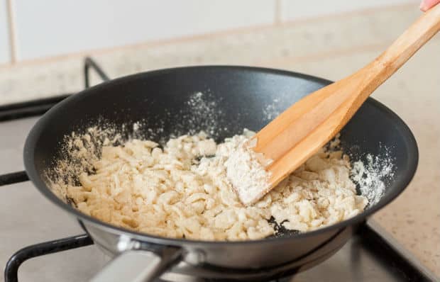 обжаренный лук с мукой на сковороде с деревянной лопаткой на плите