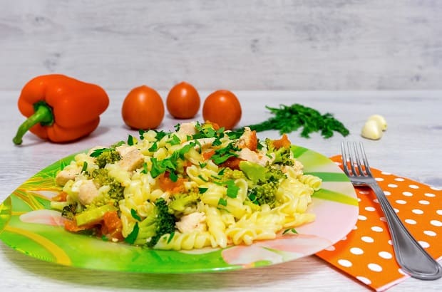 готовая паста с курицей, овощами и зеленью в тарелке, рядом филка на салфетке в горошек и помидоры на столе