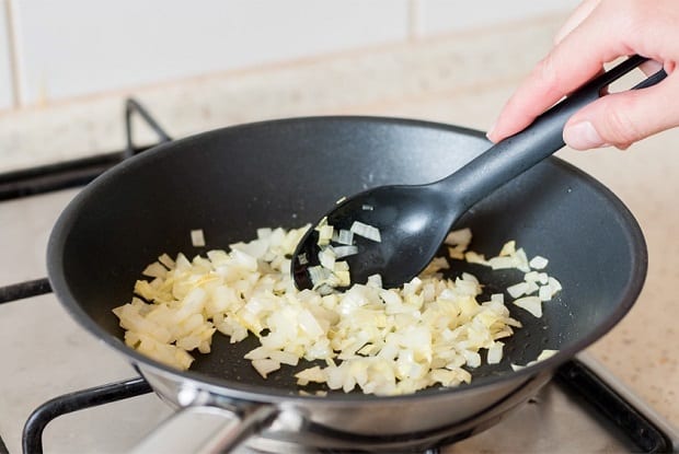 нарезанный лук с ложкой на сковороде на плите