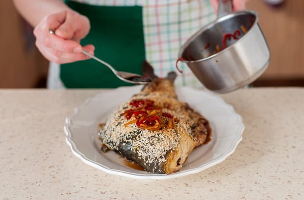 карп, запеченный целиком, посыпанный кунжутом и политый соусом из перца, на тарелке на столе