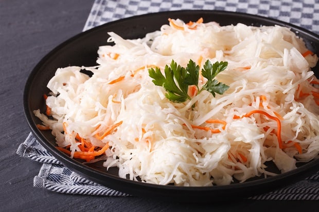 квашеная капуста с морковкой и веточкой петрушки в черной тарелке на столе, застеленном кухонным полотенцем