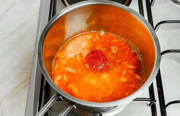 порция томатной пасты в сотейнике с бульоном и чечевицей на плите