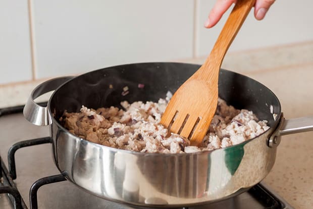 кусочки обжаренного куриного филе с деревянной лопаткой в сковороде на плите
