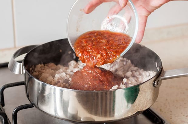 аджика добавляется в сковороду с кусочками обжаренного куриного филе