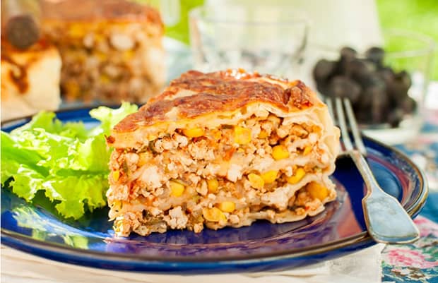 треугольный кусочек запеканки с курицей, овощами и кукурузой на тарелке с листьями салата
