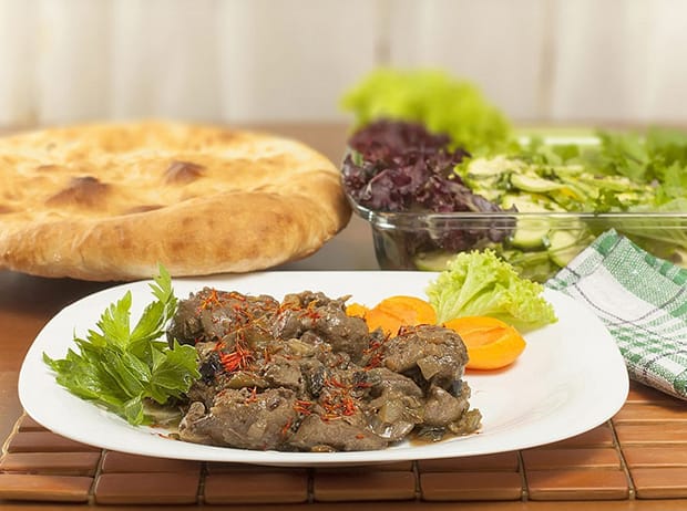 куриная печень с овощами и зеленью на тарелке, рядом лаваш