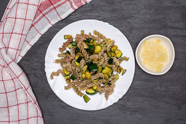 вареные макароны с кабачками на тарелке, кусочки сыра в пиале