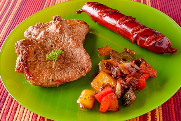 свиная отбивная с овощами и сосиской на тарелке
